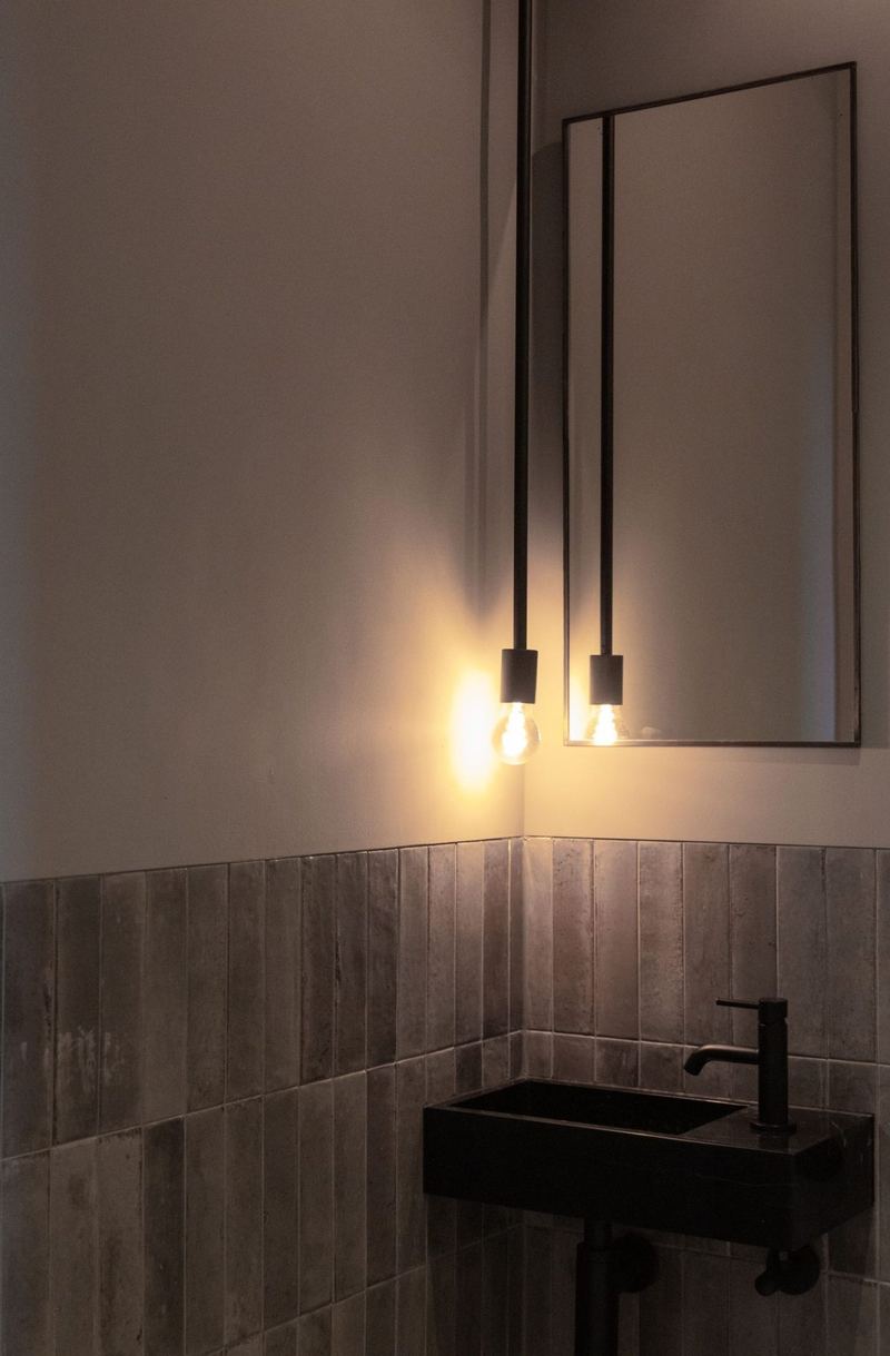 Toilet met staande tegels, zwart fonteintje en hanglampen