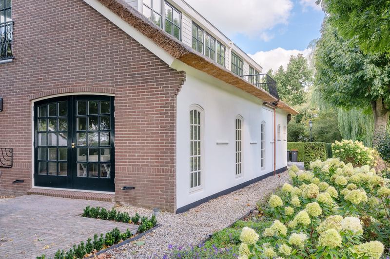 Witte vleugel met boogramen en donkergroene tuindeuren
